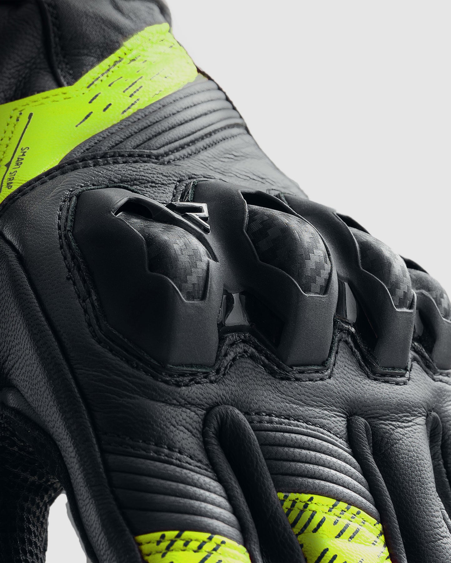 Close-up of a black and gray glove with knuckle protection and yellow accents on a light gray background